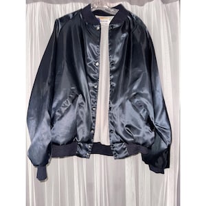 May include: A navy blue satin bomber jacket with a white interior. The jacket has a button-up front, a ribbed collar, cuffs, and hem. The jacket is hanging on a clear hanger against a white curtain.