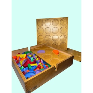 May include: Wooden educational toy set with a box filled with colorful geometric shapes. The set includes a wooden lid with circular cutouts and a separate wooden board with more circular cutouts. The shapes are various colors and sizes.
