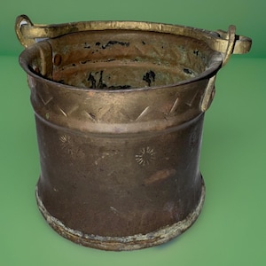 May include: Antique brass bucket with a handle. The bucket has a cylindrical shape with a slightly flared base. Decorative starburst and geometric patterns are etched around the body. The handle is attached to the rim with small loops.