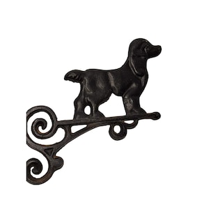 May include: Black cast iron dog-shaped bracket with a decorative scroll design. The dog is standing on a horizontal bar, and the bracket has a curved arm with a scrolled end. A charming accent for any home.