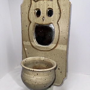 May include: A ceramic wall planter featuring an owl design and a small mirror. The planter is beige with brown speckles and has a small pot attached to the bottom.
