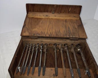 May include: A wooden box with a hinged lid containing a set of 12 drill bits. The box is open and the drill bits are visible in their slots.