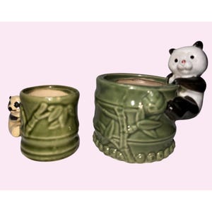 May include: Two ceramic panda bear planters. The planters are green with bamboo leaf designs. One planter has a small panda bear attached to the side. The other planter has a larger panda bear attached to the side. The planters are suitable for small plants.