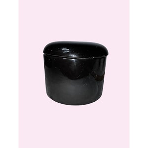 May include: A small, black ceramic container with a matching lid. The container has a glossy finish and a rounded shape. The lid fits snugly on top, creating a smooth, seamless look. The container is likely used for storage or decoration.