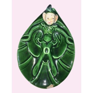 May include: A vintage ceramic figurine of a smiling elf with a green outfit and hat. The elf is set against a green, leaf-shaped background. The figurine has a glossy finish and is likely a decorative item.