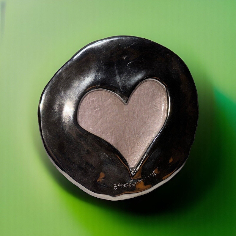May include: A silver-toned, heart-shaped dish with a textured, dark outer rim and a lighter, smooth heart-shaped interior. The dish sits on a green surface. The text "Barefoot Days" is visible on the bottom right.