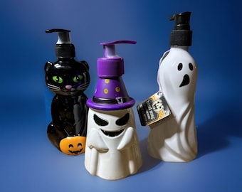 Peut inclure: Trois distributeurs de savon pour les mains sur le thème d'Halloween. Une bouteille en forme de chat noir avec une citrouille, un fantôme blanc avec un chapeau de sorcière violet et un fantôme blanc avec une pompe noire. Les bouteilles sont sur fond bleu.