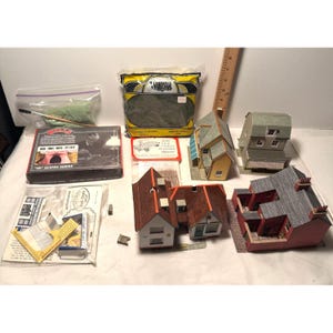 Può includere: Una collezione di kit per modellismo ferroviario e accessori, tra cui una scatola della serie scenica Wills, un sacchetto di fogliame verde, un righello di legno e diverse strutture in miniatura assemblate con tetti rossi, gialli e grigi.