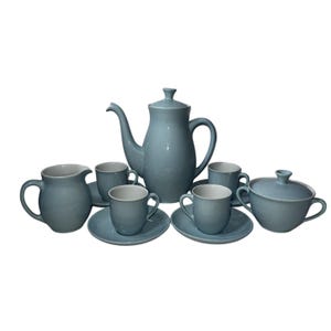 May include: A complete blue ceramic tea set. The set includes a teapot, creamer, sugar bowl with lid, six teacups, and six saucers. The interior of the cups and creamer are white. The set is arranged on a white background.