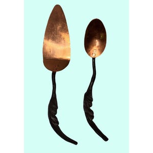 May include: A copper-colored pie server and spoon set. The serving pieces have dark, curved handles with a leaf-like design. The pie server has a triangular blade, while the spoon has a rounded bowl.