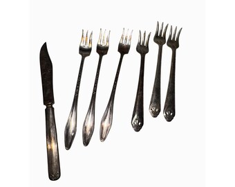 May include: An assortment of antique silverware, including a knife and several forks. The knife has a curved blade and ornate handle. The forks have long, slender tines and decorative detailing on the handles. The silverware is silver-toned.