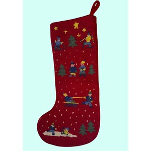May include: Red Christmas stocking with embroidered winter scene. The stocking features skiers, trees, and snowflakes. The top has a red loop for hanging. The design includes yellow, blue, and green accents.