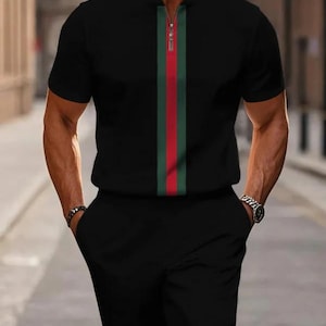 May include: Black short-sleeved shirt and matching shorts with a vertical green, red, and white stripe down the center. The shirt has a zipper.