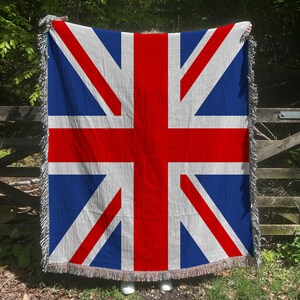 Pode incluir: Uma manta tecida com a Union Jack, a bandeira nacional do Reino Unido. A manta apresenta um fundo azul com listras vermelhas e brancas que se cruzam e uma borda com franjas.