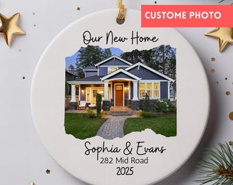 May include: A white ceramic ornament with a gold hanging cord. The ornament features a photo of a house with the text "Our New Home", "Sophia & Evans", "282 Mid Road", and "2025". A red banner reads "CUSTOM PHOTO".