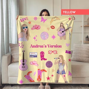 May include: A yellow blanket featuring illustrations of a woman, musical notes, hearts, cowboy boots, and the text "Andrea's Version". The blanket has a variety of pink and purple accents.