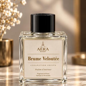 Puede incluir: Un frasco cuadrado de vidrio para fragancia de hogar con una tapa cilíndrica negra. La etiqueta presenta el texto AÉRA ROUEN, Brume Veloutée, COLLECTION PRIVÉE, Parfum d'intérieur, Fragrance de Grasse y Fabriqué en Normandie en letras marrón oscuro.