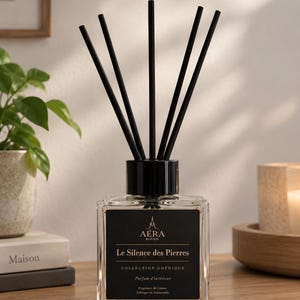 May include: A clear glass reed diffuser bottle with a black cap and five black reeds. The black label features the text AÉRA ROUEN, Le Silence des Pierres, COLLECTION GOTHIQUE, Parfum d'intérieur, Fragrance de Grasse, Fabriqué en Normandie.