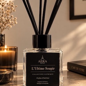 Op de afbeelding: Een vierkante glazen geurstokjesfles met een zwarte dop en zwarte rietjes. Het zwarte etiket bevat de tekst AÉRA ROUEN, L'Ultime Soupir, COLLECTION GOTHIQUE, Parfum d'intérieur, Fragrance de Grasse en Fabriqué en Normandie.