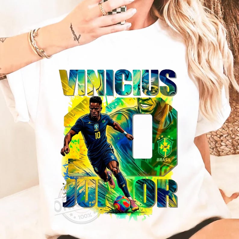 May include: White t-shirt featuring a graphic of a soccer player in a blue uniform, with the name "VINICIUS JUNIOR" in bold letters. The design includes the number 10 and the Brazilian flag colors.