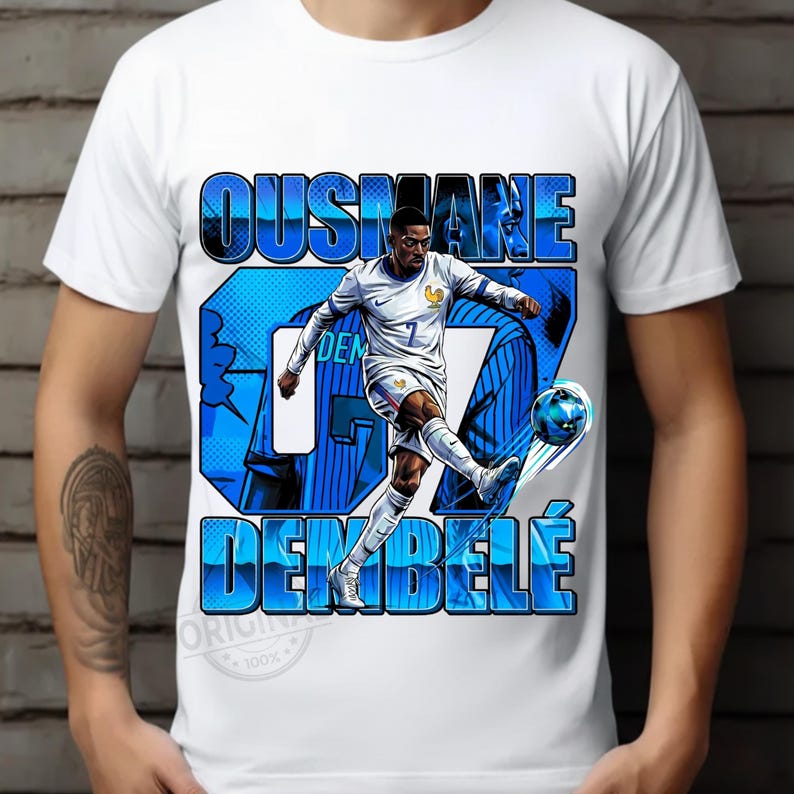 May include: White t-shirt featuring a graphic of soccer player Ousmane Demb&eacute;l&eacute; in action, kicking a soccer ball. The design includes the player's name and jersey number in blue, with a French flag detail.