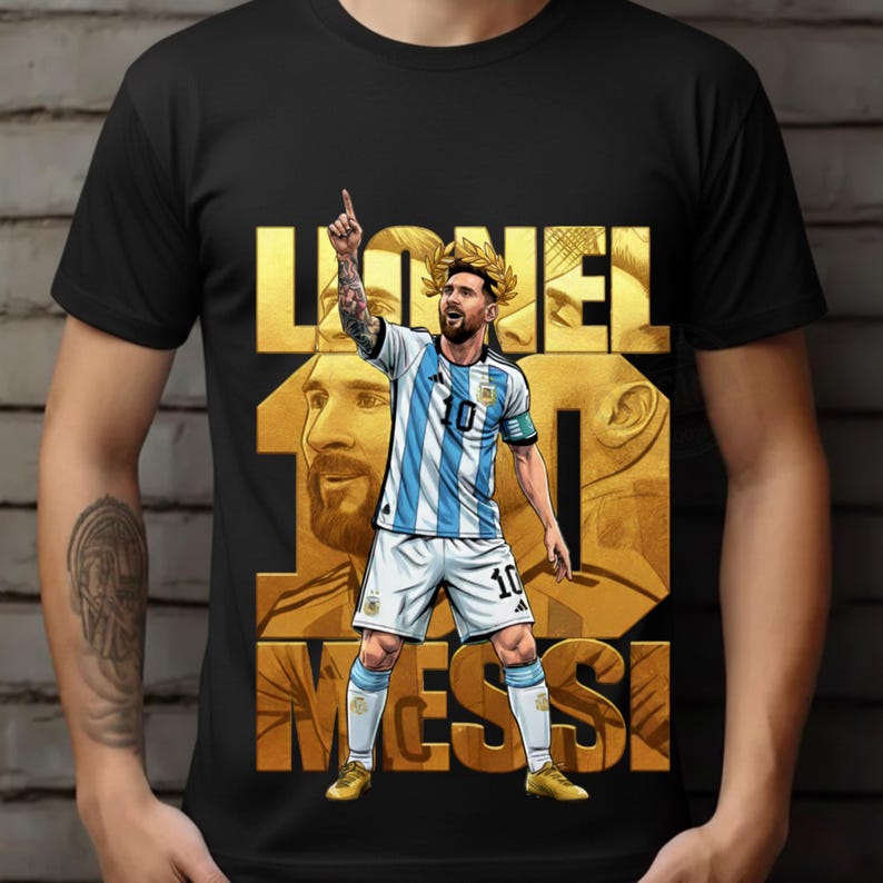 May include: Black t-shirt featuring a graphic of Lionel Messi in his Argentina soccer uniform, with the number 10. The design includes the name "Lionel Messi" in gold lettering and a gold laurel wreath.