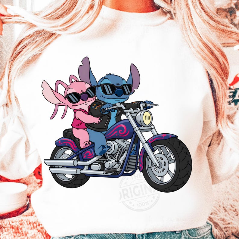 May include: White sweatshirt featuring a graphic of two cartoon characters, one blue and one pink, riding a motorcycle. The blue character wears a black leather jacket and sunglasses. The motorcycle is blue and purple.