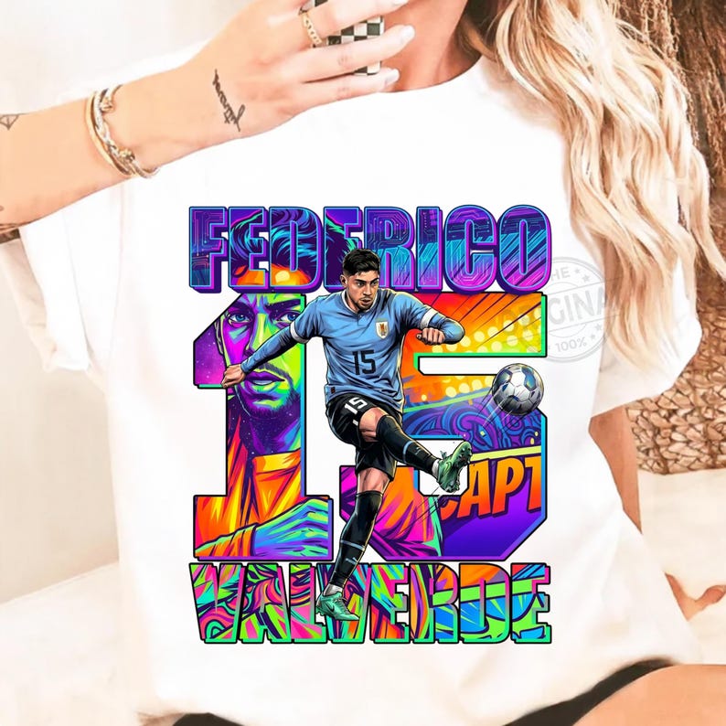 May include: White t-shirt featuring a colorful graphic of a soccer player kicking a ball. The design includes the name "FEDERICO VALVERDE" and the number "15" in vibrant, stylized lettering. The player is wearing a light blue jersey.