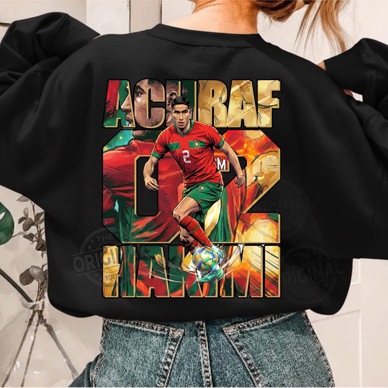 May include: Black sweatshirt featuring a graphic of a soccer player in a red and green uniform, with the name "ACHRAF" and the number "02" in large letters. The design includes the word "MAXIM" and a soccer ball.