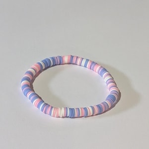 Könnte beinhalten: Ein Armband aus kleinen, bunten Perlen. Die Perlen sind in einem Muster aus Rosa, Weiß und Hellblau angeordnet.
