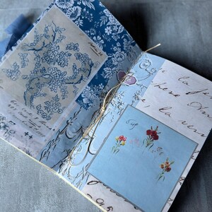 May include: Open journal with blue floral and script patterned pages. The journal is bound with a twine string. A light blue square features small floral illustrations and the word "Bye".