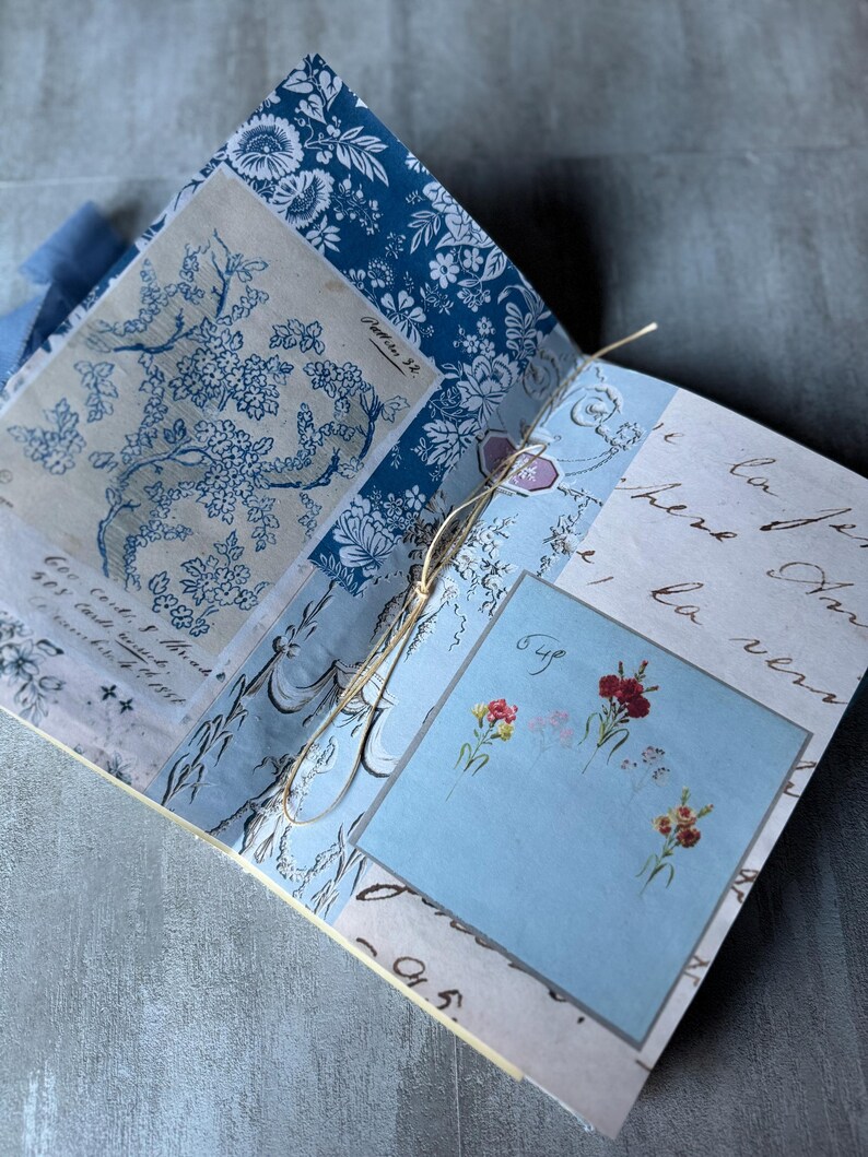 May include: Open journal with blue floral and script patterned pages. The journal is bound with a twine string. A light blue square features small floral illustrations and the word "Bye".