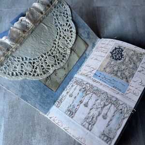 May include: Open journal with blue and white patterned pages, featuring a lace doily and handwritten script. The journal has a vintage aesthetic, with a delicate, layered design. The pages display architectural drawings and decorative elements.