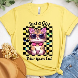 May include: Yellow t-shirt featuring a cartoon cat wearing sunglasses and a pink bow. The cat is set against a black and white checkered background with the text "Just a Girl Who Loves Cat".
