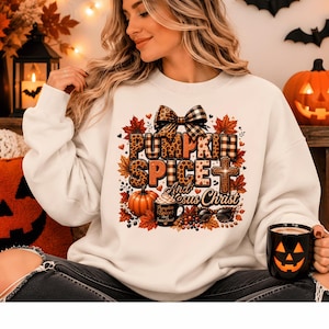 Peut inclure: Un sweat-shirt blanc à col rond avec une impression graphique portant le texte "PUMPKIN SPICE And Jesus Christ". Le motif comprend un nœud à imprimé léopard, des feuilles d'automne, une citrouille, une tasse, une croix et des lunettes.