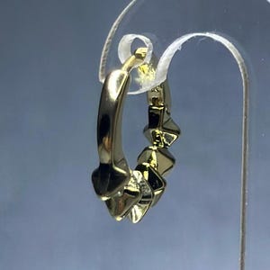 May include: Gold hoop earrings with a geometric design. The earrings are made of a smooth, shiny metal and have a series of small, triangular shapes around the hoop.