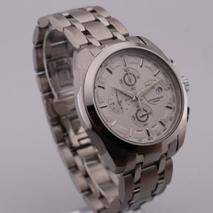 May include: A silver-toned chronograph watch with a matching stainless steel band. The watch face is light gray with three sub-dials and silver hands. The watch is a stylish accessory.