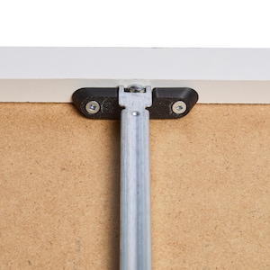 May include: Close-up of a white table leg with a black metal bracket and screws. The leg is made of metal and is attached to the table top with a bracket.