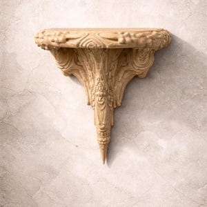 May include: A beige, ornate wall shelf with a decorative design. The shelf has a rounded top with carved details and a pointed, stylized support. The text "DIGITAL STL FILE" is at the top.