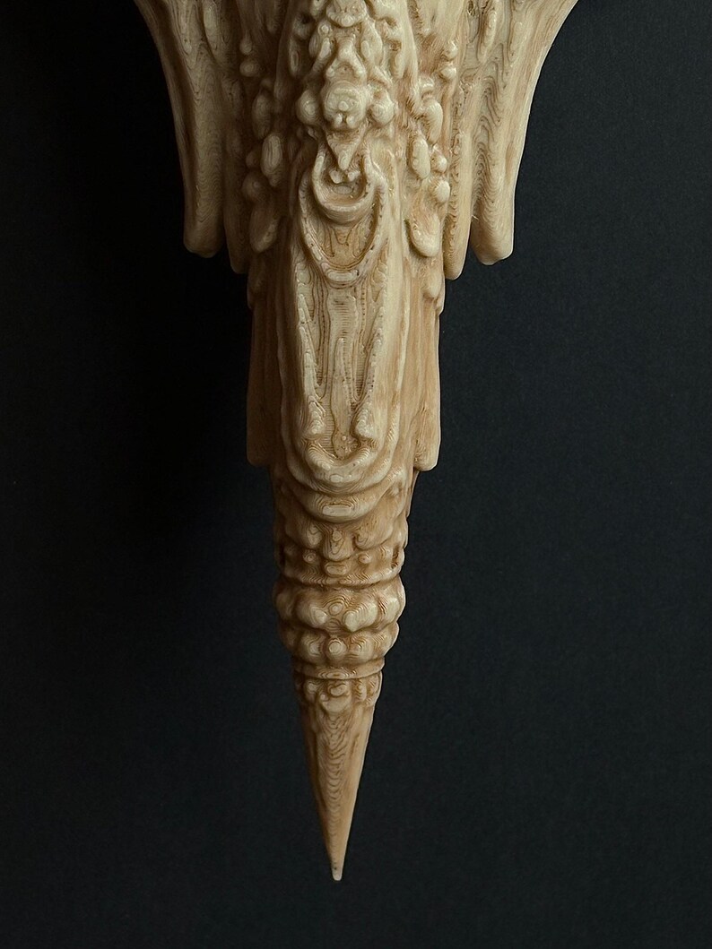 May include: A detailed, light-colored, carved wooden sculpture with a textured surface. The sculpture has an ornate design with a pointed bottom and a complex, layered structure. The background is a solid, dark color.