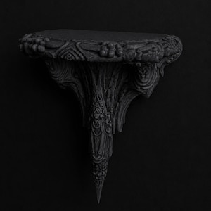 May include: Ornate black wall shelf with a detailed, carved design. The shelf has a rounded top with floral and foliate patterns, supported by a stylized, tapering base. The overall aesthetic is gothic and decorative.