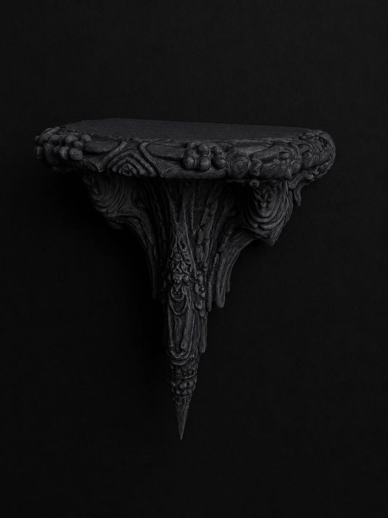 May include: Ornate black wall shelf with a detailed, carved design. The shelf has a rounded top with floral and foliate patterns, supported by a stylized, tapering base. The overall aesthetic is gothic and decorative.