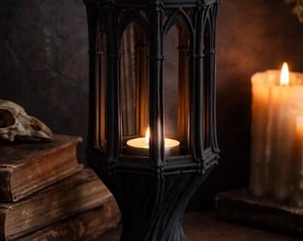 May include: A black gothic-style candle lantern with a lit candle inside. The lantern has an arched design and sits on a wooden surface. The text "DIGITAL STL FILE" is at the top of the image. The background includes old books and a lit candle.
