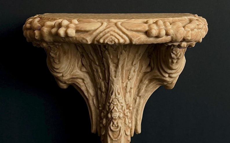 May include: Ornate, beige-colored wall shelf with detailed floral and leaf carvings. The shelf has a rounded top and a decorative, sculpted support. The design is reminiscent of classical architecture.