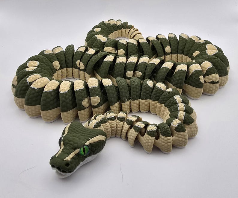 Puede incluir: Escultura detallada de una serpiente en tonos verdes y beige. El cuerpo de la serpiente est&aacute; segmentado, con un patr&oacute;n texturizado. La cabeza presenta ojos verdes y un dise&ntilde;o detallado, creando una apariencia realista. La escultura se exhibe sobre una superficie blanca.