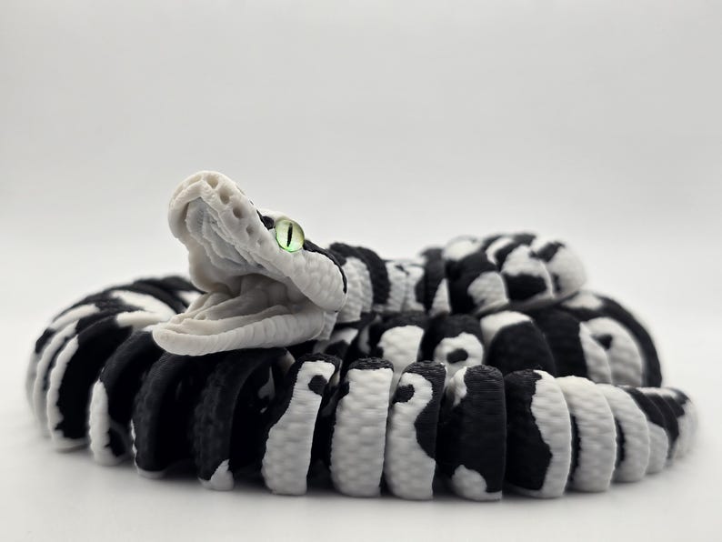 Puede incluir: Escultura detallada de una serpiente con la boca abierta. El cuerpo de la serpiente es negro y blanco, con un patr&oacute;n de rayas y manchas alternas. La cabeza de la serpiente es blanca, con una textura detallada y un ojo verde.