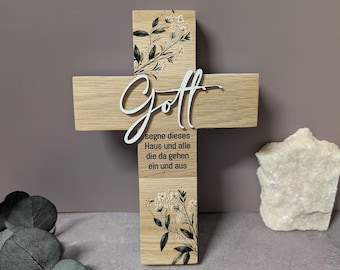Könnte beinhalten: Ein helles Holzkreuz mit dem weißen Schriftzug Gott und dem schwarzen Text segne dieses Haus und alle die da gehen ein und aus. Das Kreuz ist mit schwarz-weißen botanischen Blumenillustrationen auf dem Holz verziert.