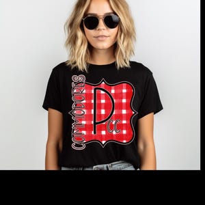 May include: Black t-shirt featuring a red and white checkered design with the letters "P CC" and the word "COMMODORES" in white. The shirt is worn by a person wearing sunglasses.