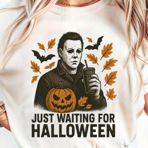 以下が含まれることがあります： ハロウィーンをテーマにしたグラフィックがプリントされた白いTシャツ。デザインは、飲み物を持った男性、ジャック・オ・ランタン、コウモリ、秋の葉が特徴です。「JUST WAITING FOR HALLOWEEN」の文字が下にプリントされています。
