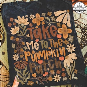 May include: Black t-shirt with the text "Take Me To The Pumpkin Patch" in brown and orange lettering. The shirt is decorated with floral and pumpkin graphics in shades of brown, orange, and cream.
